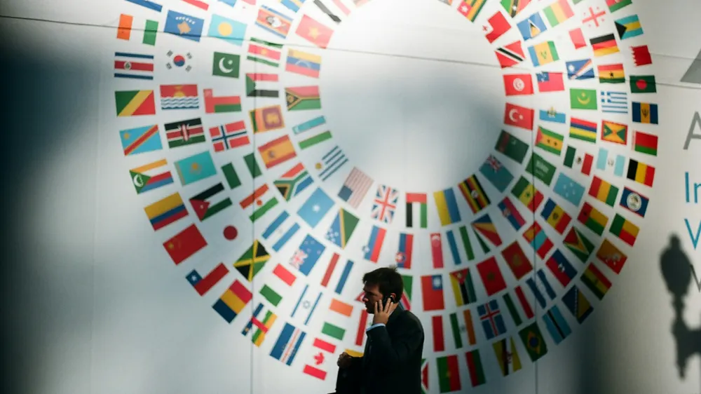 Geschäftsmann telefoniert vor einer Wand mit Flaggen vieler Länder – internationale Kommunikation mit Dolmetscher